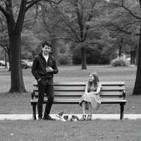 ONE MALE STAND AND ONE GIRL SIT IN BANCH IN PARK IMAGE ALL IN BLACK AND WHITE